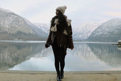 Full length of woman standing by lake against mountain during winter