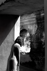 Side view of woman looking through window at abandoned building