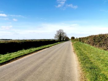 Empty road amidst field against sky