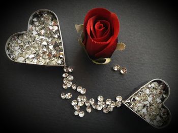 Close-up of diamonds in heart shape container by rose on table