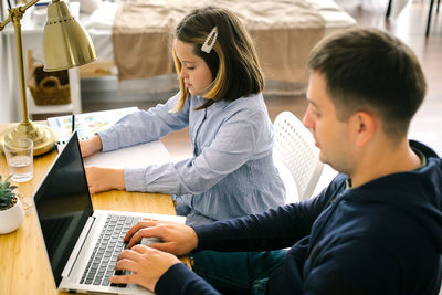 Side view of man using laptop sitting by girl at home