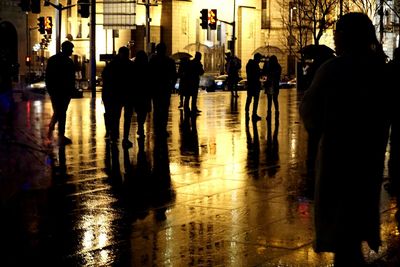 Silhouette people walking on illuminated street in city