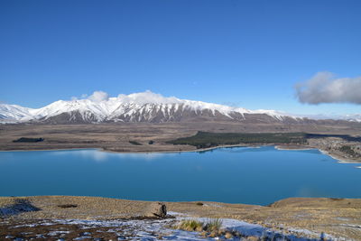 Scenic view of lake by snowcapped mountain against blue sky
