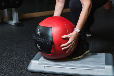 Crop anonymous senior female athlete in sports clothes leaning forward while taking medicine ball during workout in gymnasium