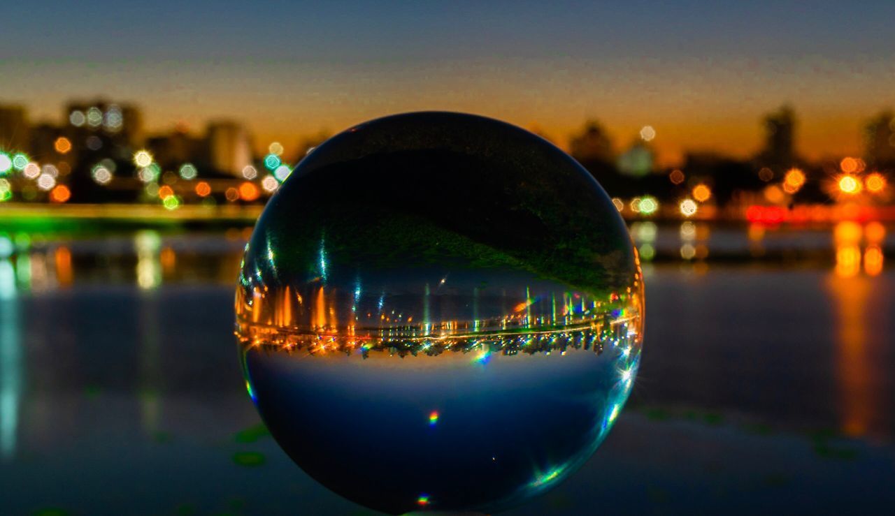 CLOSE-UP OF ILLUMINATED GLASS AGAINST RIVER AT NIGHT