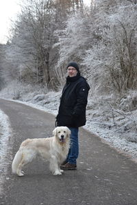 Portrait of man with dog standing on road during winter