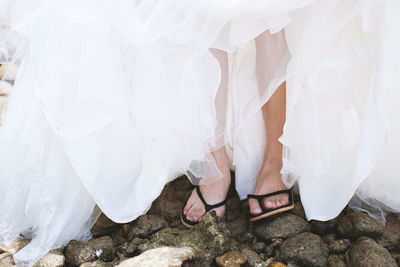 Low section of woman in wedding dress wearing flip-flops