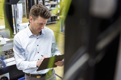 Man with clipboard in factory taking notes