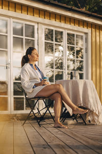 Thoughtful mature woman drinking coffee while sitting at patio in holiday villa