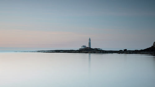 Lighthouse amidst sea and buildings against sky