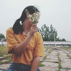 Woman holding flowers while sitting against clear sky