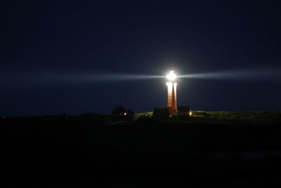 Illuminated lighthouse by building against sky at night