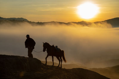 People riding horses on mountain against sky during sunset