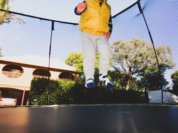 Low angle view of boy jumping over trampoine against building