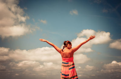 Man with arms outstretched standing against sky