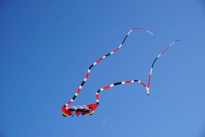 Low angle view of kites flying against clear blue sky