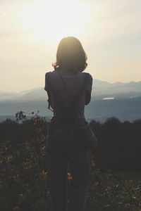 Rear view of woman standing on field against sky during sunset