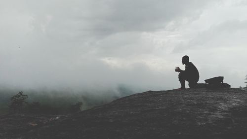 Man standing on rock looking away against sky