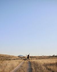 Rear view of woman on dirt road amidst grassy landscape against clear sky