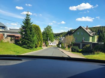 Street amidst trees and houses against sky