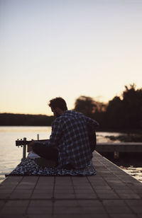 Man sitting on pier over lake against clear sky