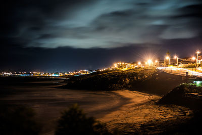 Illuminated cityscape by river against sky at night