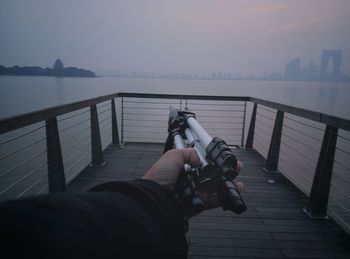 Close-up of man holding camera on railing against sea