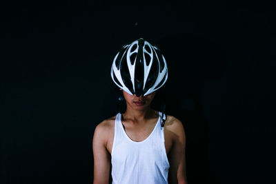 Young woman wearing sports helmet while standing against black background