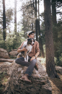 Man with australian shepherd sitting on rock in forest