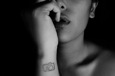 Cropped image of young woman with tattooed hand against black background