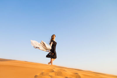 Full length of woman standing on sand dune against clear sky