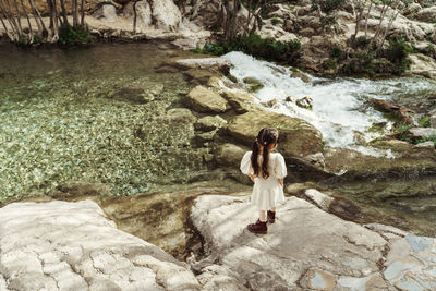 Rear view of girl standing on rock and looking on water 