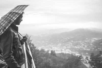 Side view of man with umbrella looking at landscape