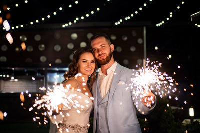 Portrait of happy bridegroom holding sparklers at night