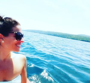 Young woman wearing sunglasses standing by sea against clear sky