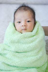 High angle portrait of cute baby boy wrapped in towel lying on bed at home