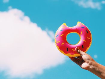 Cropped hand of person holding inflatable donut against sky