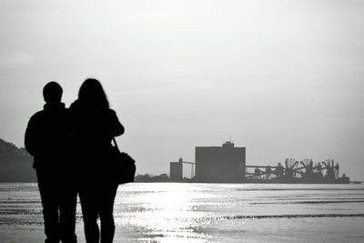 Silhouette couple against sea in city against clear sky
