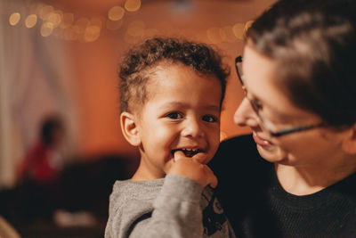 Close-up of mother with cute son against illuminated christmas lights at home