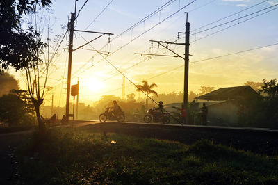 People at railroad crossing against sky during sunset