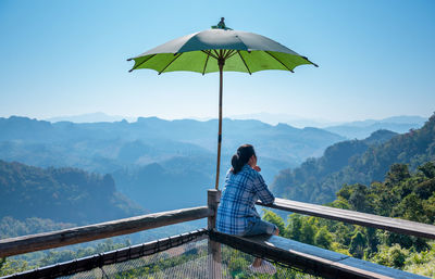 Rear view of man sitting on mountain against sky