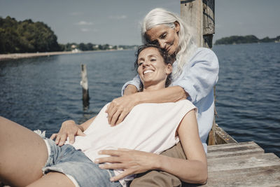 Mother and daughter sitting on jetty, relaxing at the sea