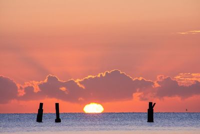 Silhouette wooden posts in sea against sky during sunset