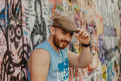 Young man looking away while standing against graffiti wall