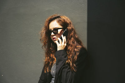 Portrait of young woman wearing sunglasses standing against wall