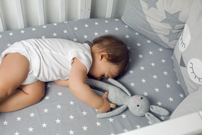 One year old baby boy lying in a round bed with a knitted rabbit toy and sleeping
