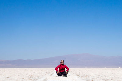 Full length of man sitting on land against clear blue sky