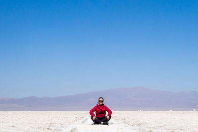 Full length of man sitting on land against clear blue sky