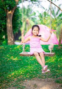 Portrait of smiling girl sitting on swing in park