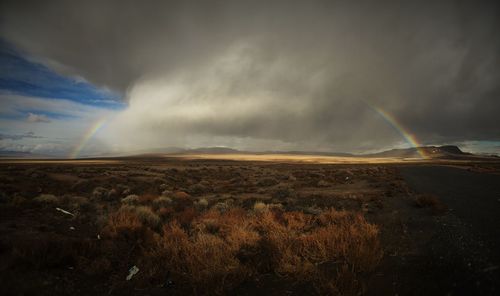 Scenic view of rainbow over field against cloudy sky